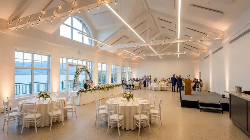 Paddlewheel Hall set for a wedding, with string lights across the vaulted ceiling, a flowered head table in front of the lake windows and round guest tables